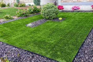 Small front yard with artificial grass surrounded by shrubs and flowers